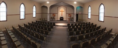 An empty church hall filled with empty chairs and a lit cross at the end with an altar