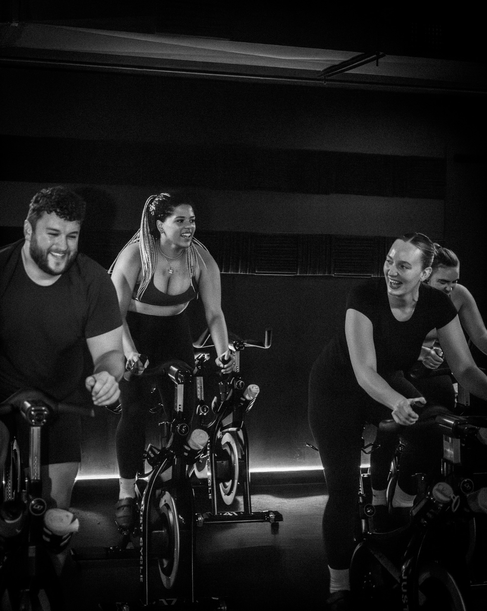 A black and white photo of a spin class and people laughing on bikes