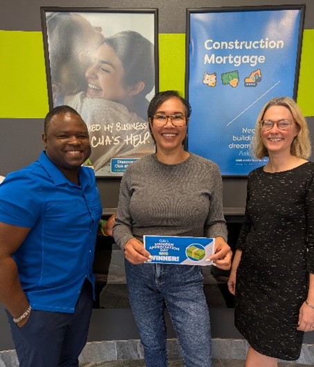 A woman smiles in the middle of two CUA staff holding a Winner envelope for CUA Member Appreciation Day