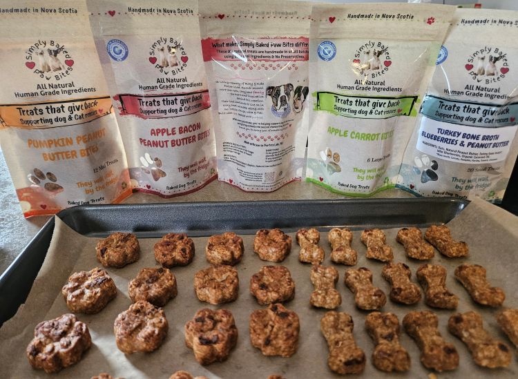 a row of five different types of dog treat bags in a row behind a cookie sheet with treats fresh out of the oven.